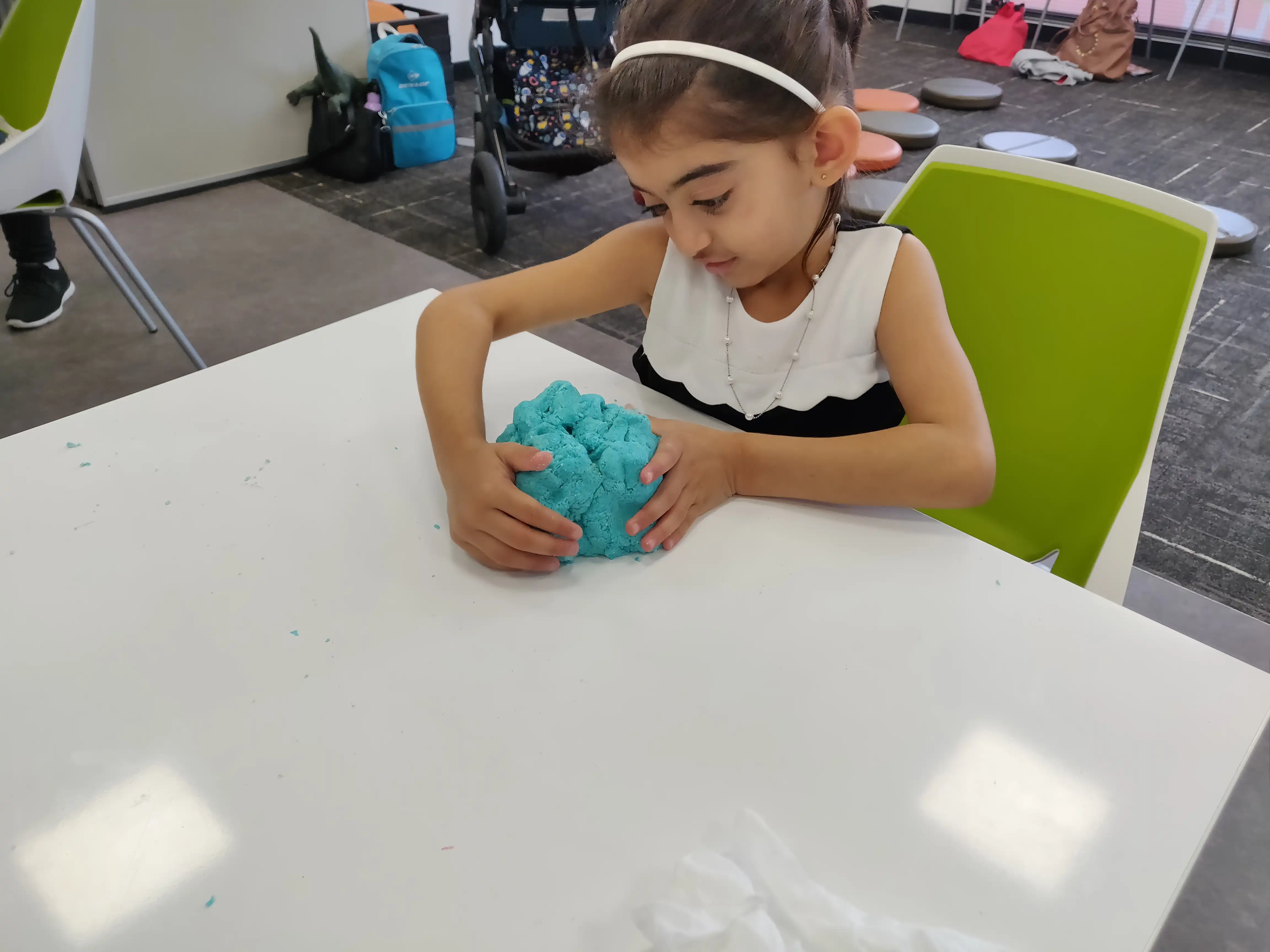 Child playing with blue playdough at desk.